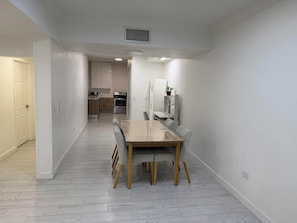 Una cocina moderna con electrodomésticos de acero inoxidable, un comedor con mesa y sillas de madera, y un pasillo que conduce a una puerta.