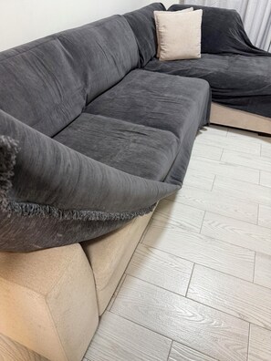 Ein Ecksofa mit einem Farbdesign aus Beige und Dunkelgrau, auf einem hellen Holzboden platziert.