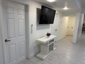 A hallway with white doors, a mounted flat-screen TV, a white console table with a small plant, and a light-colored wooden floor. - Casa Viena: Comfort, Privacy, and 24/7 Self-Check-In (Juárez)