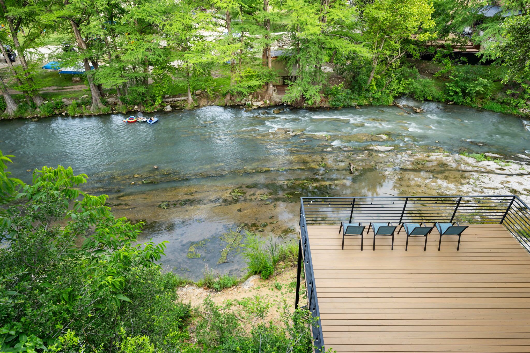 Ein Fluss mit klarem Wasser, umgeben von üppigem Grün und einer Holzterrasse mit Stühlen.