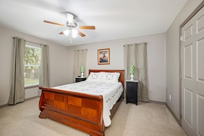 A bedroom with a wooden bed, a ceiling fan, two bedside tables, and a window with curtains. - Guadalupe Horseshoe Hideaway CL 320 (Canyon Lake)