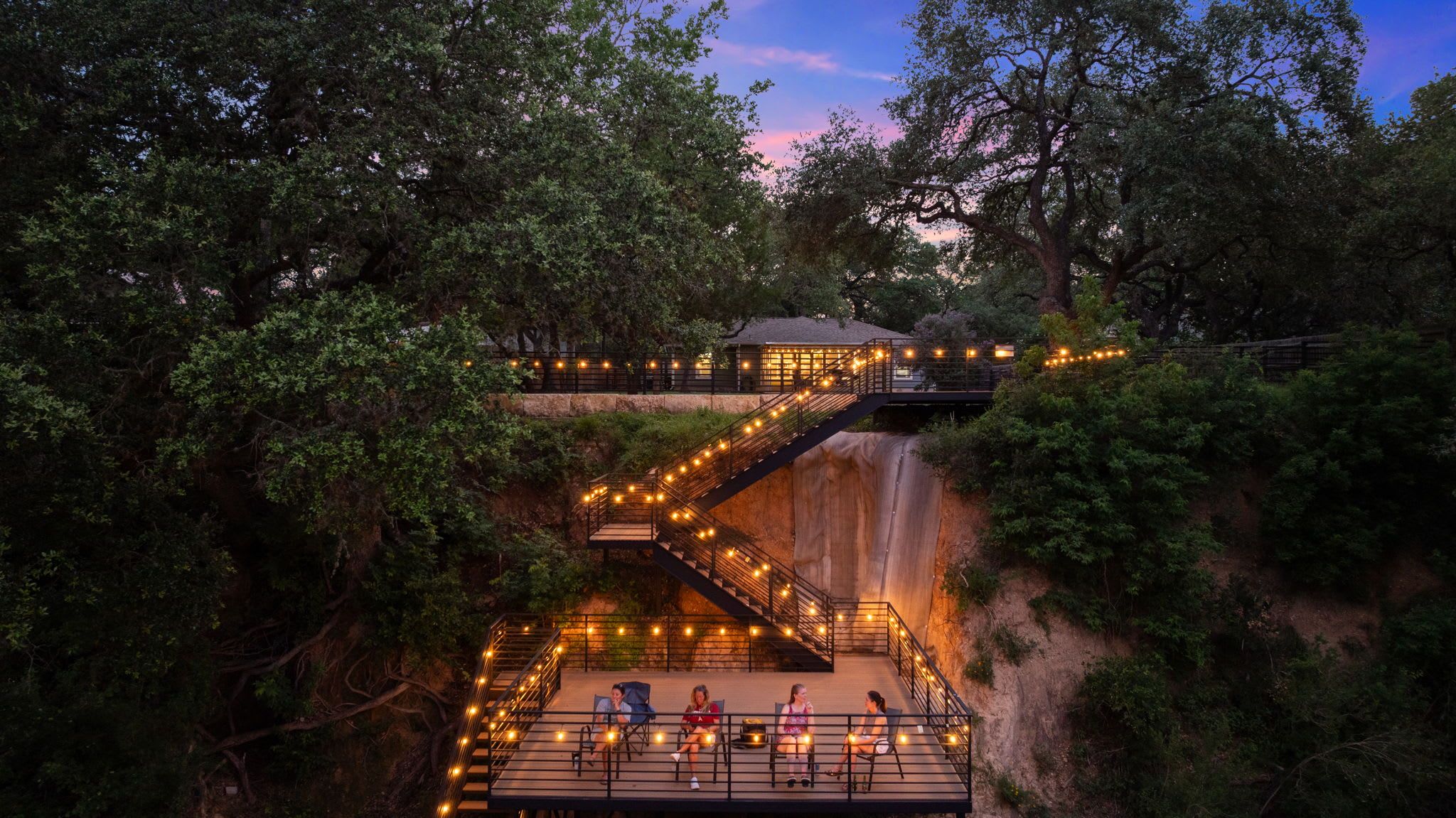 A multi-level outdoor area with a waterfall, wooden walkways, and string lights.