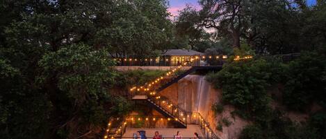 A multi-level outdoor area with a waterfall, wooden walkways, and string lights.