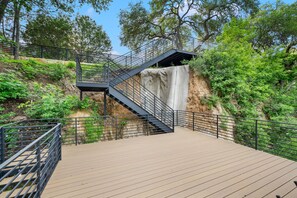 Eine Holzterrasse mit einer Metalltreppe, die zu einem Wasserfall führt.