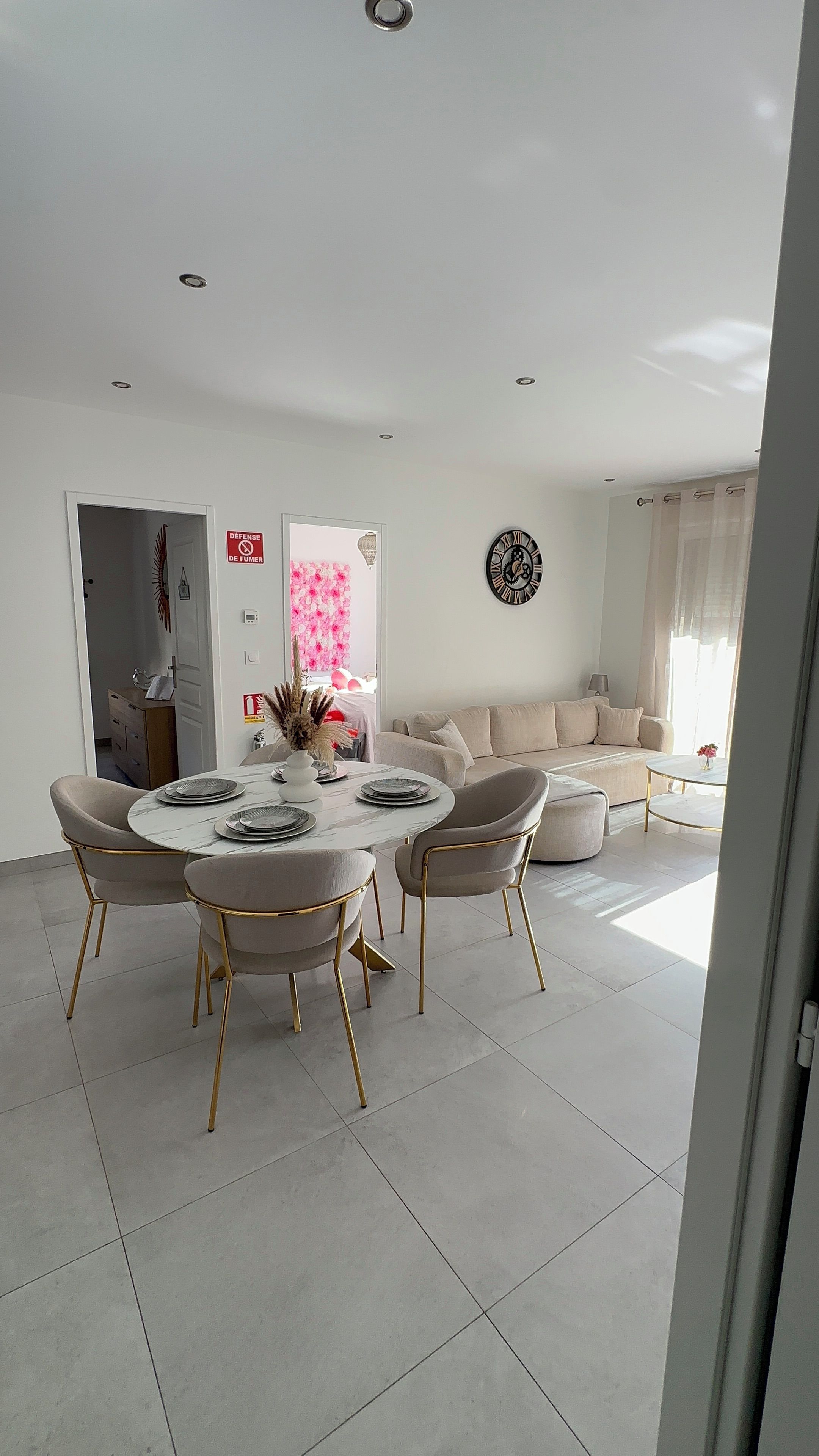 A modern living room with a round dining table, beige sofas, and a decorative wall clock.