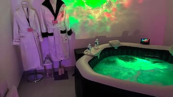 A spa room with a heart-shaped light projection on the wall, a hot tub, and two robes on a rack.