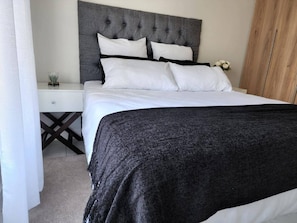 A neatly made bed with a grey headboard, white bedding, and a dark grey throw blanket. - Lovely One-bedroom Unit With Pool and Gym Facilities in Stand (Cape Town)