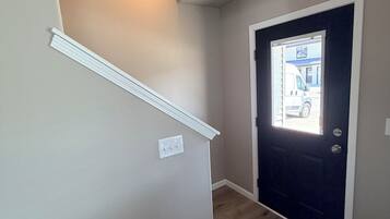 A hallway with a wooden floor, a dark door, and a light switch on the wall.