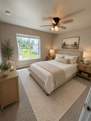 A bedroom with a large bed, bedside tables, a ceiling fan, a window with a view, and a painting on the wall. - 3-bedroom townhome -8 Miles From Downtown Iowa City (Hills)