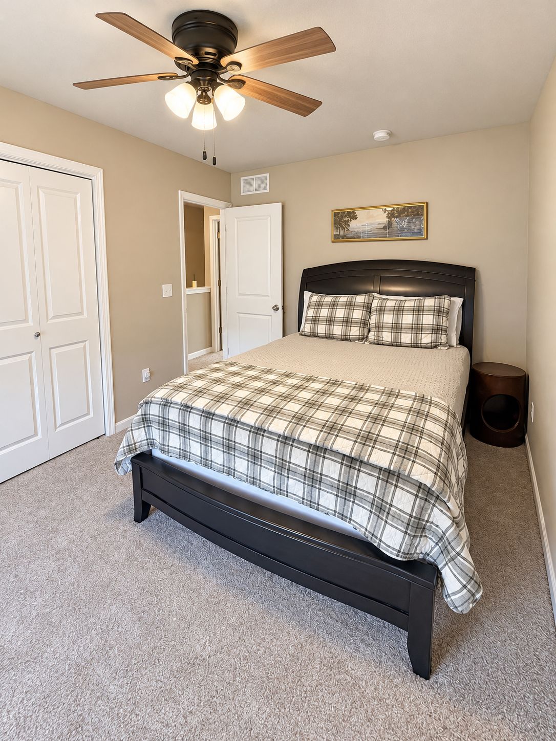 A bedroom with a bed, a ceiling fan, a door, and a small bedside table.