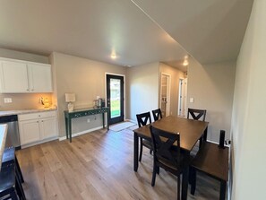 A spacious kitchen with white cabinets, a wooden dining table, and chairs. There is a black door leading to a hallway. - 3-bedroom townhome -8 Miles From Downtown Iowa City (Hills)