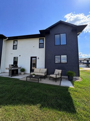 A two-story house with a garage, a patio with outdoor furniture, and a lawn.