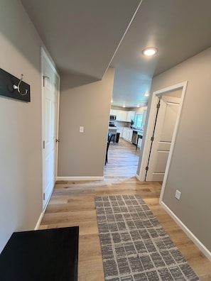 A hallway with a wooden floor, a patterned rug, and a door leading to a kitchen area.
