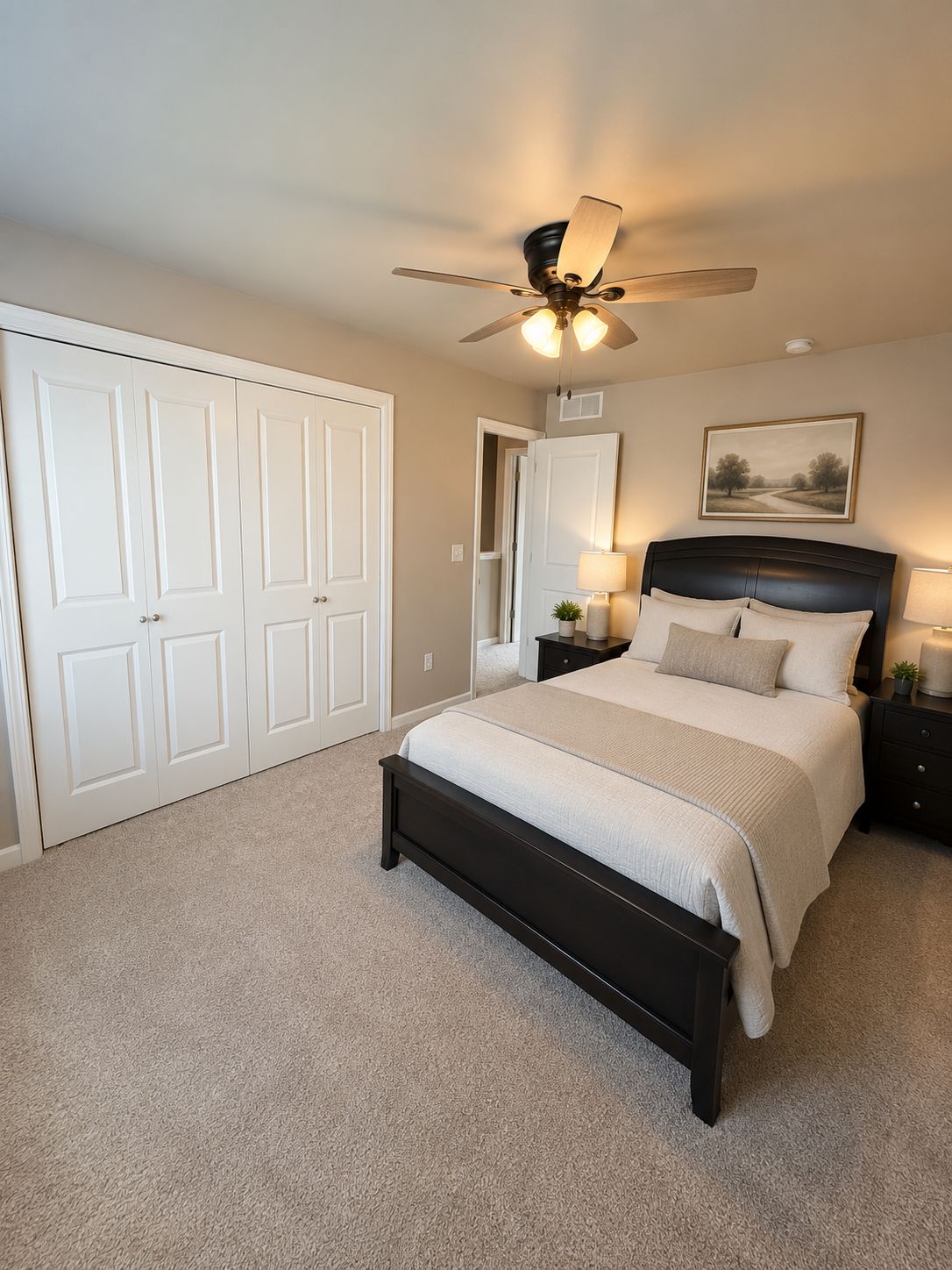 A bedroom with a bed, bedside tables, a ceiling fan, a door, and a framed picture on the wall.