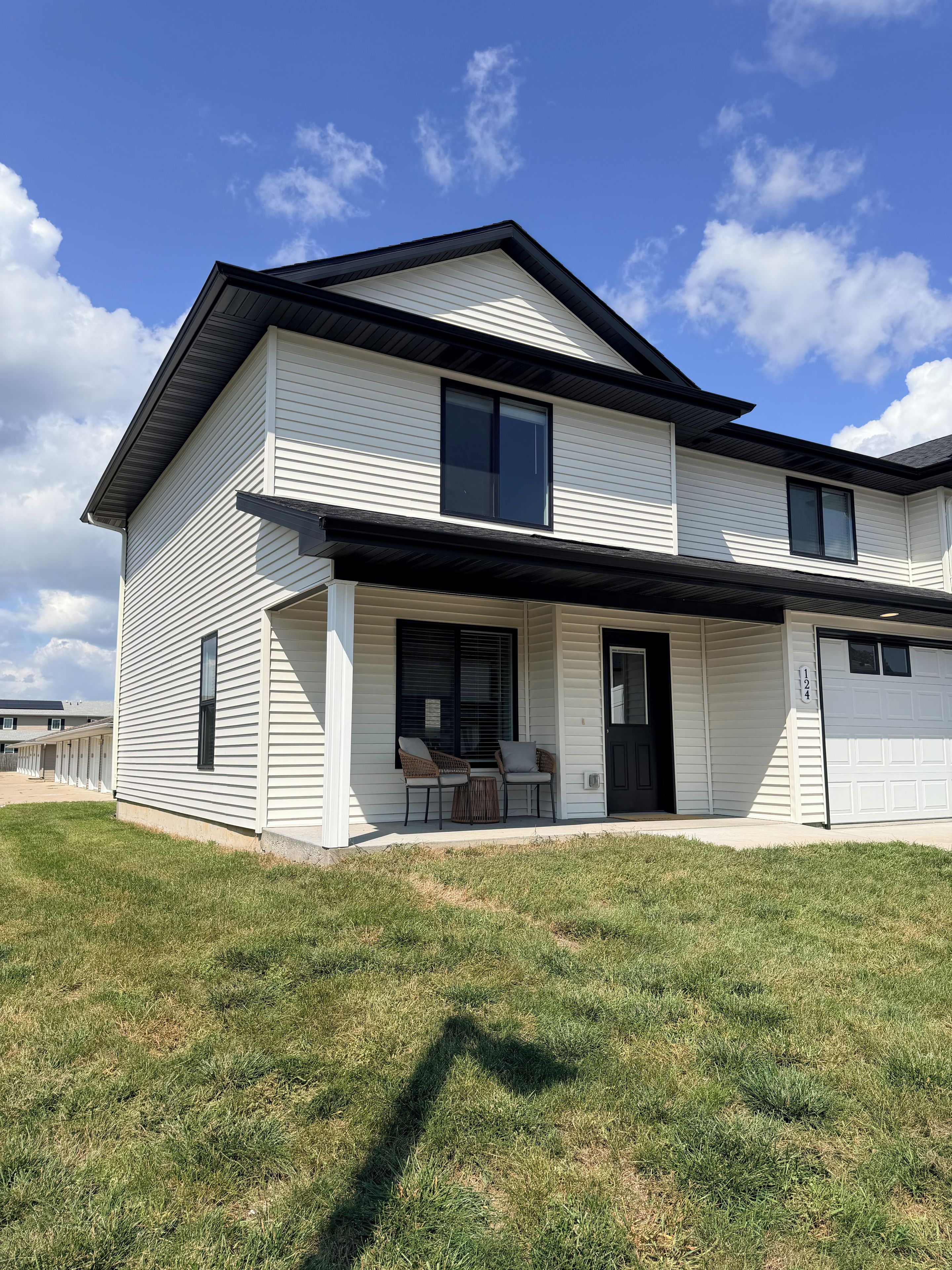 A two-story residential building with a covered porch, a garage, and a well-maintained lawn.