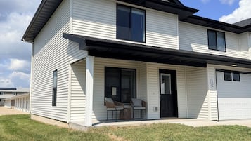 A two-story residential building with a covered porch, a garage, and a well-maintained lawn.