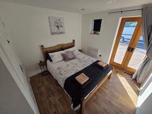 A bedroom with a wooden bed, a nightstand, a wall-mounted radiator, and a window with a view. - Luxury 2-Bed New Forest Retreat with Paddocks, Animals (Dogs Welcome) (Southampton)