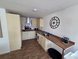 Een kleine keuken met een houten aanrecht, een wasmachine en een grote wandklok.