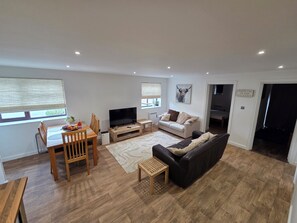 A modern living room with a dining area, a flat-screen TV, a sofa, and a coffee table. - Luxury 2-Bed New Forest Retreat with Paddocks, Animals (Dogs Welcome) (Southampton)
