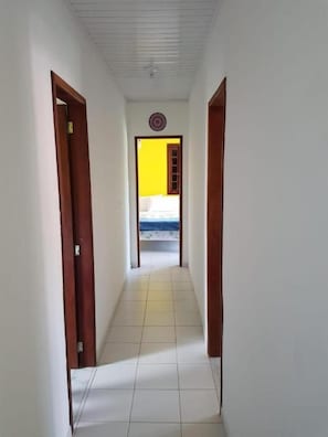 Un pasillo estrecho con suelo de baldosas blancas y puertas de madera a ambos lados.