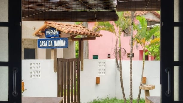 An outdoor patio area with a tiled floor, wooden tables, and chairs. There is a sign indicating the location as 'Casa da Marina.'