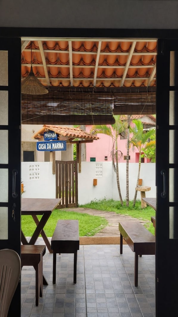 Un patio al aire libre con suelo de baldosas, mesas y sillas de madera. Un letrero indica el lugar como 'Casa da Marina'.