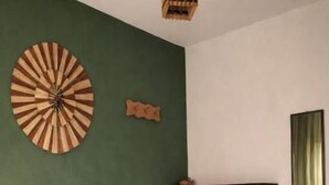 A neatly made bed with a white duvet and a patterned throw blanket, a wall clock, and a hanging light fixture.