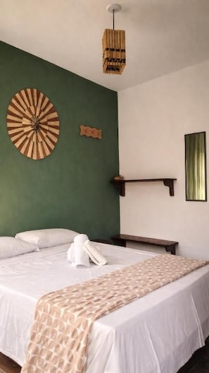 Una cama bien hecha con edredón blanco y manta decorativa, un reloj de pared y una lámpara colgante.