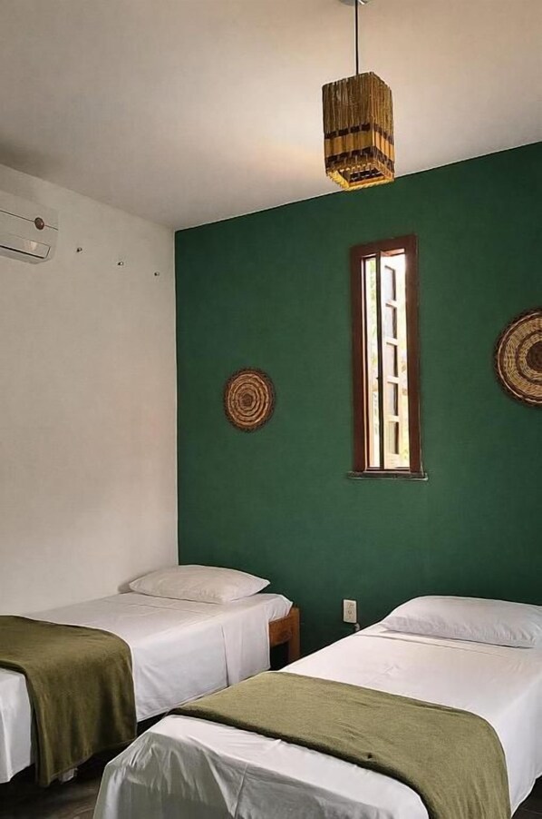 A room with two beds, a window, and a hanging light fixture.
