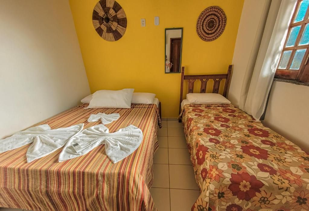 Een kamer met twee bedden, waarvan er eentje streepjesbeddengoed heeft en de ander bloemenprint. Er hangt een spiegel aan de muur en een ronde decoratie.