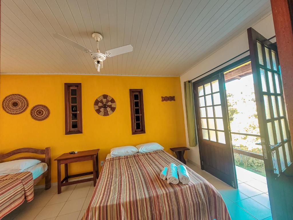 A room with a bed, two smaller beds, a ceiling fan, and a large window.