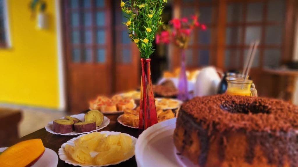 Una mesa con diversos alimentos, entre ellos un pastel de chocolate, rebanadas de fruta y un jarrón con flores.
