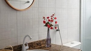 A bathroom with a white sink, a wooden-framed mirror, a vase with red flowers, and a white toilet.