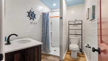 Un baño con lavamanos blanco, inodoro, ducha con cortina y decoración de timón de barco en la pared.