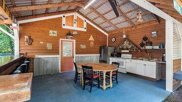 A rustic cabin interior with a dining area, kitchen, and a large window overlooking a pool.