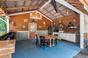 A rustic cabin interior with a dining area, kitchen, and a large window overlooking a pool.