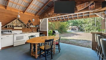 A rustic kitchen with a wooden table and chairs, a large window, and a view of the outdoors.