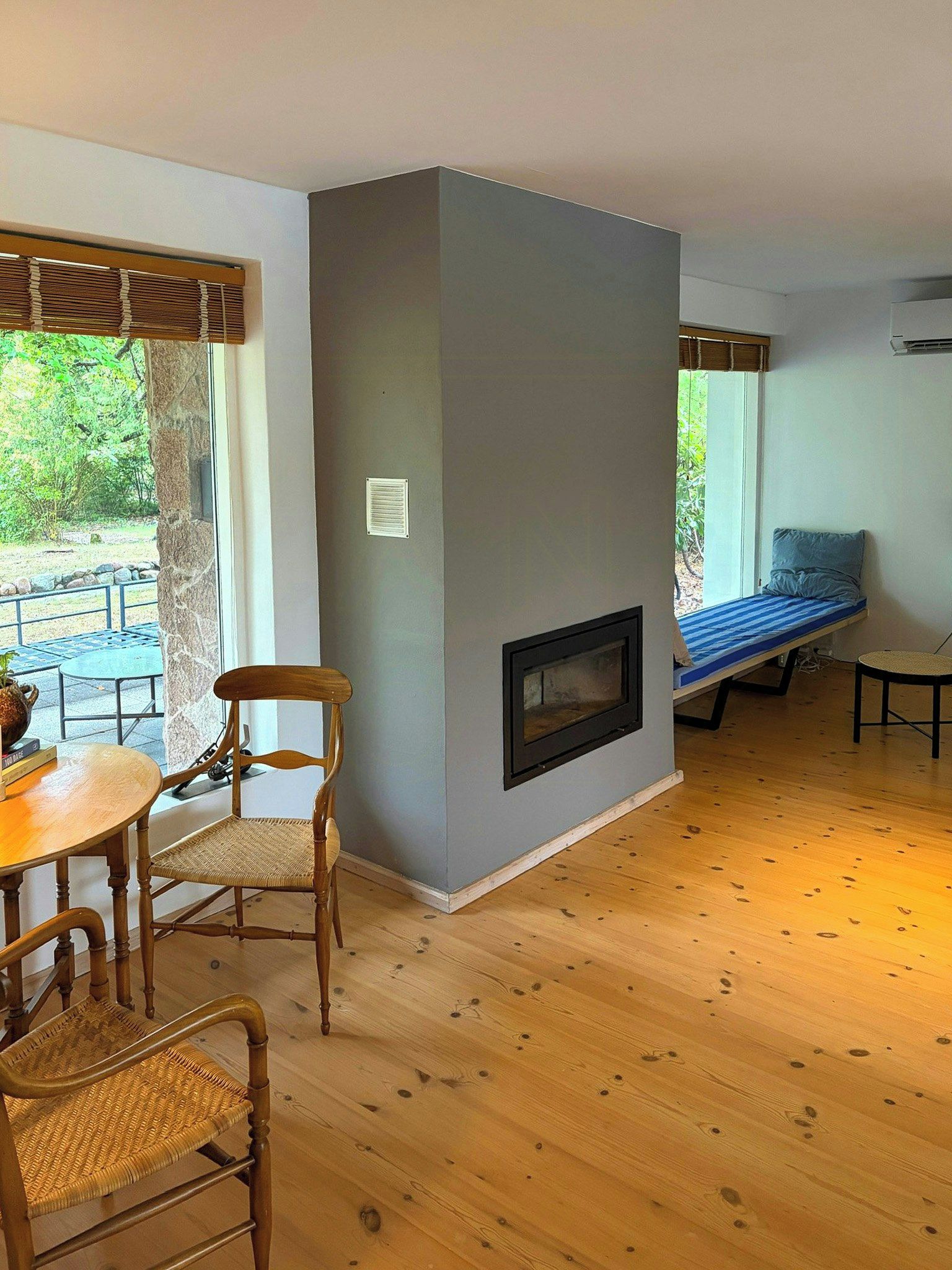 A room with a fireplace, a dining table with chairs, and a window with a view of greenery.