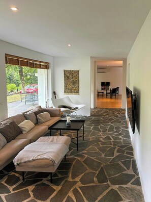 A modern living room with a stone-patterned floor, a sofa, a white chair, and a flat-screen TV mounted on the wall. - Private summer house in nature near Ebeltoft (Ebeltoft)