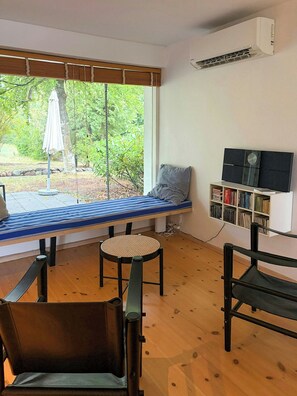 A room with a bed, a chair, a small table, a bookshelf, and a window with blinds. - Private summer house in nature near Ebeltoft (Ebeltoft)