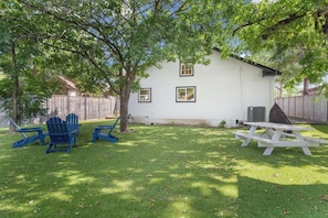 A backyard with a white house, a wooden fence, a tree, and outdoor furniture including blue chairs and a picnic table. - Modern Home Near Downtown Georgetown (Georgetown)