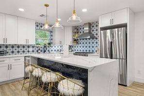 A modern kitchen with white cabinets, a marble island, bar stools, pendant lights, and a stainless steel refrigerator. - Modern Home Near Downtown Georgetown (Georgetown)