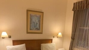 A hotel room with two beds, a headboard, bedside lamps, a painting on the wall, and a window with curtains. - Waterloo Hotel (Newport)