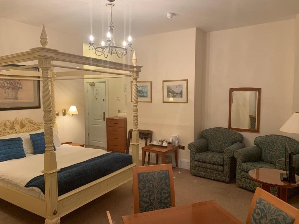 A four-poster bed with a chandelier, a sitting area with two armchairs, and a small table.