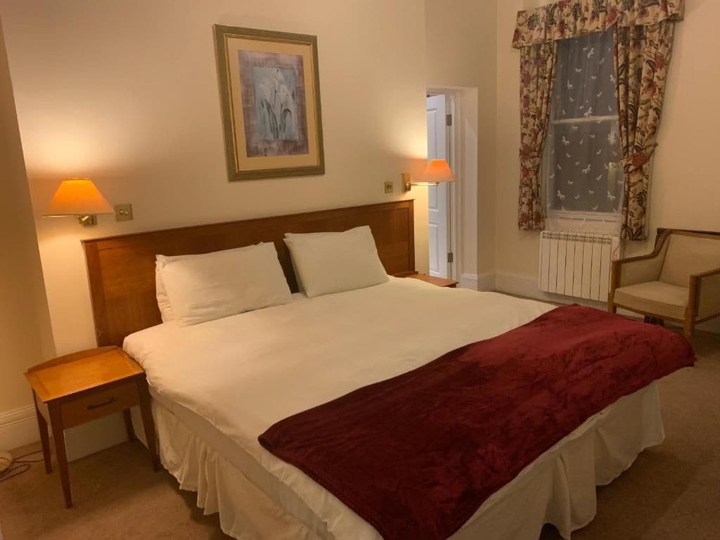 A hotel room with a large bed, two bedside lamps, a nightstand, a chair, and a window with curtains.