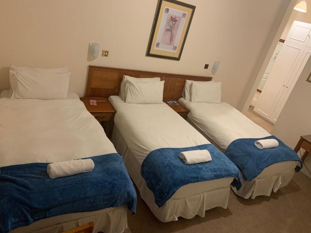 Ein Hotelzimmer mit drei Einzelbetten, jedes mit einem blauen Handtuch und weißer Bettwäsche.