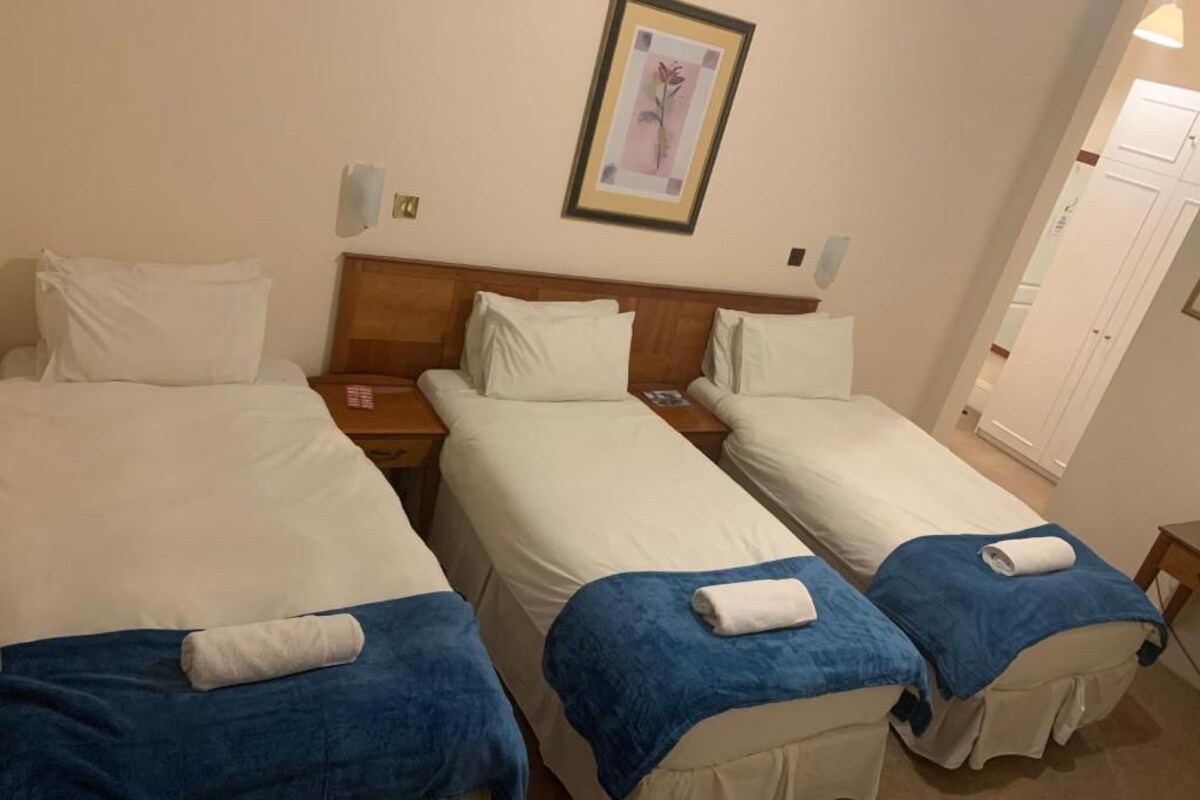 Une chambre d’hôtel avec trois lits simples, chacun équipé d’une serviette bleue et de draps blancs.