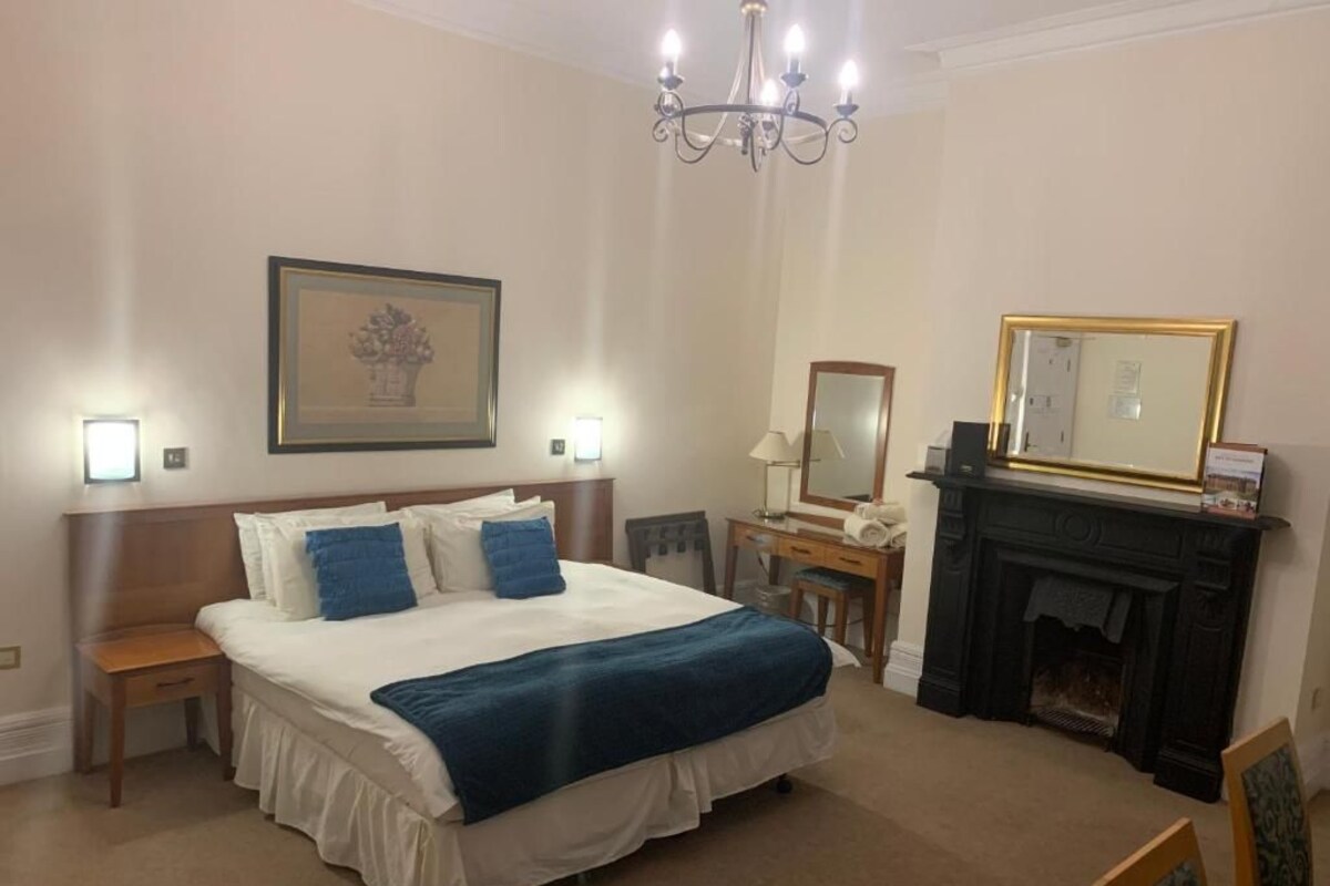 Une chambre d’hôtel avec un grand lit, des tables de chevet, une cheminée et un lustre.