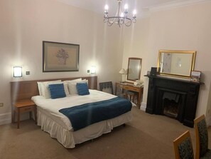 Una habitación de hotel con una cama grande, mesitas de noche, chimenea y un candelabro.