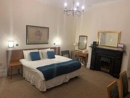 Una habitación de hotel con una cama grande, mesitas de noche, chimenea y un candelabro.